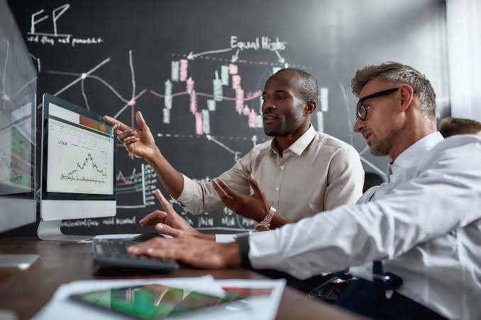 Two people examining market charts on screen, representing scrutiny of an investment offer